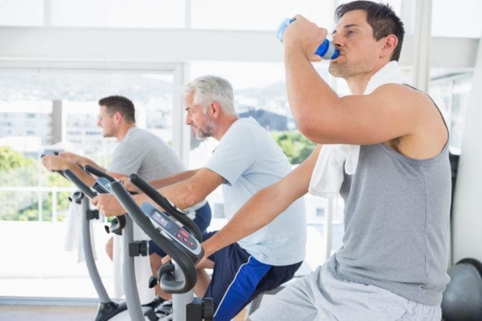 Three men, one of them older, on exercise bikes at gym