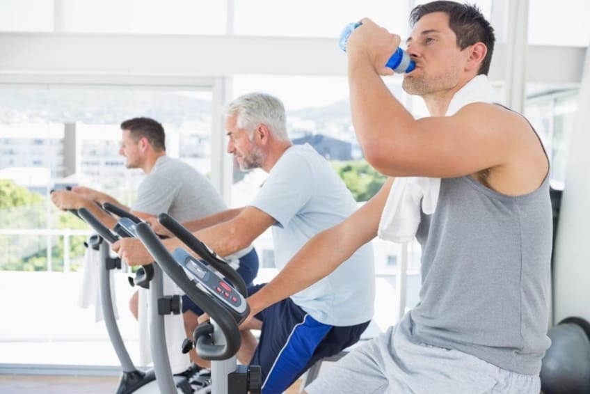 Three men, one of them older, on exercise bikes at gym