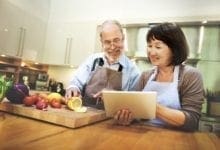 Older couple standing at counter, preparing a meal with healthy fruits and vegetables
