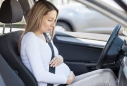 A pregnant woman holds her belly during a contraction while sitting in a car