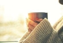 woman's hands holding hot cup of coffee or tea in morning sunlight