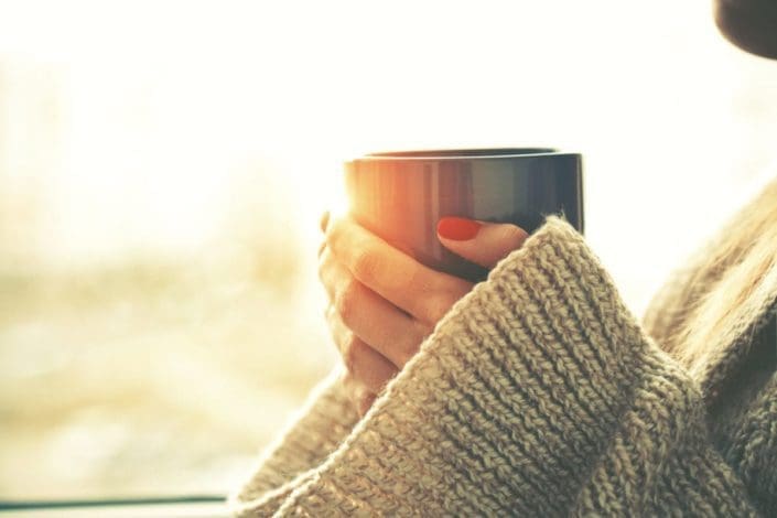 woman's hands holding hot cup of coffee or tea in morning sunlight