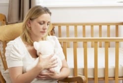 A sad woman holds a teddy bear in an empty nursery. An early pregnancy loss is a miscarriage that occurs on its own during the first 20 weeks of the pregnancy.