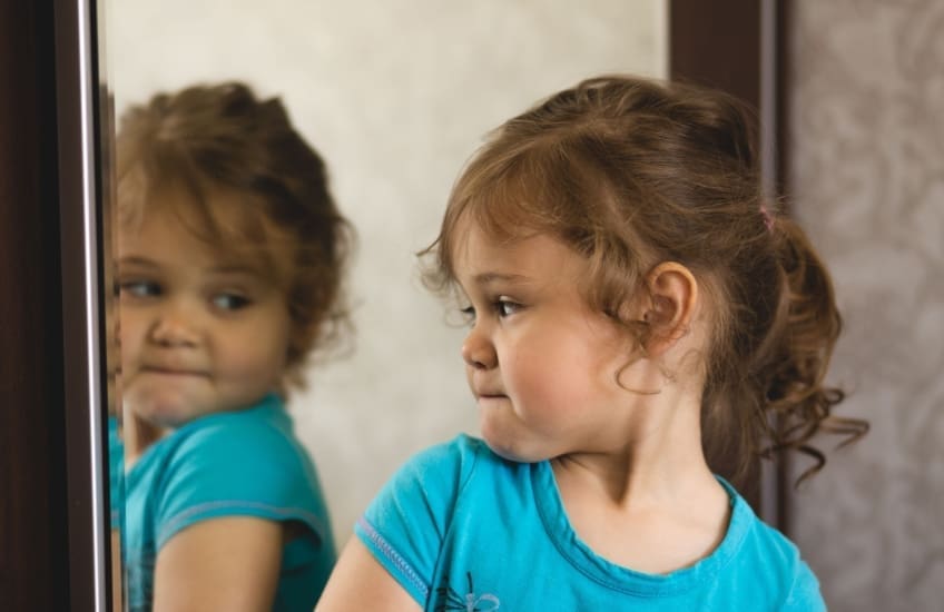 Young girl looking at her reflection in the mirror