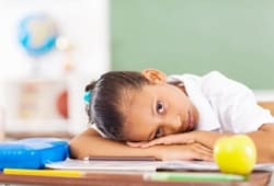 young girl rests her head on her desk at school