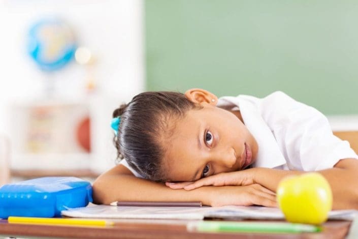 young girl rests her head on her desk at school