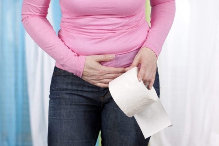 A woman with abdominal pain holding a roll of toilet paper