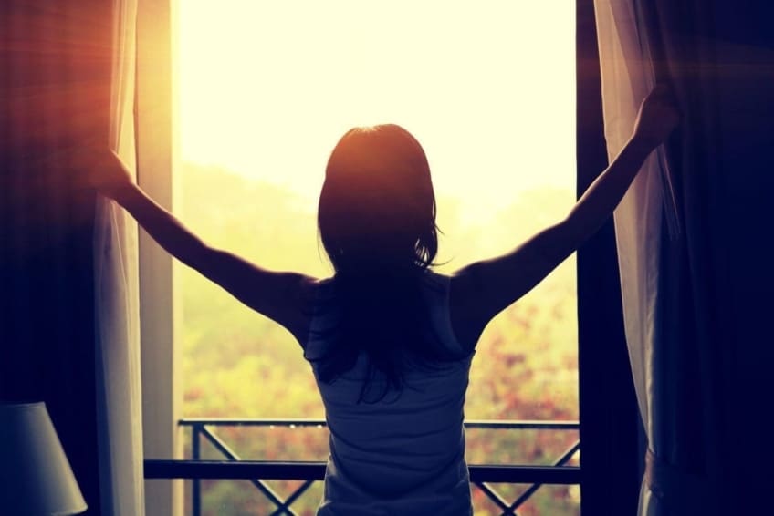 woman holding open curtains and looking out window