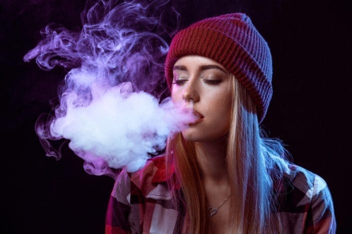 A photo of a teenage girl blowing smoke while juuling