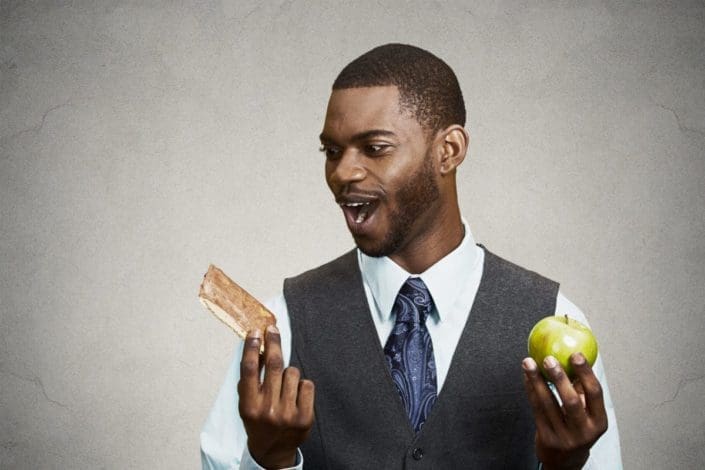 man holding an apple and a cookie, trying to choose one