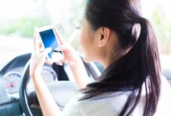 young woman texting message on mobile phone while driving car