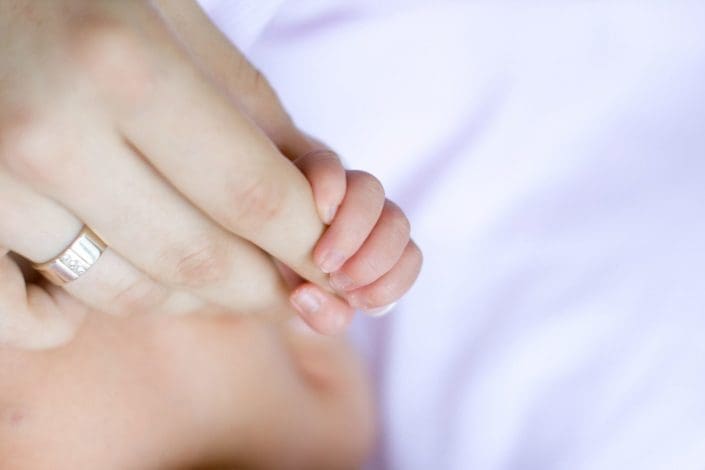 close-up of infant’s hand holding mother’s finger
