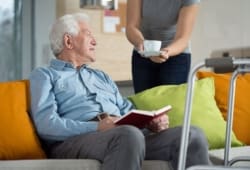 caregiver brings senior man a cup of coffee