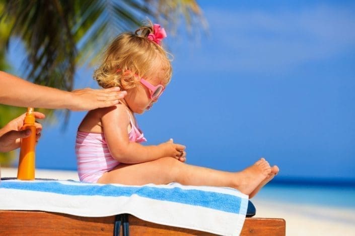 A mother applies sunscreen to her little girl’s shoulder at the beach