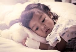 A sick little girl lies in a hospital bed. Knowing when to take your child to the emergency room can be a difficult decision, but there are things you can look for to make it easier.