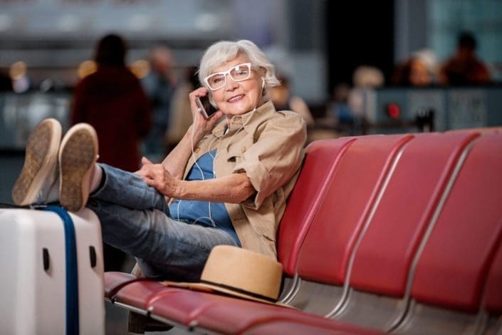Senior woman with her feet propped up on her suitcase, talking on her cell phone while waiting for her flight