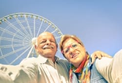 A senior couple taking a “selfie” in front of a Ferris wheel