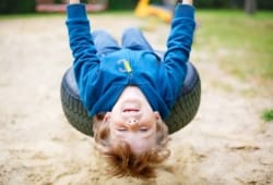 Preschool boy playing on a tire swing, leaning back as far as he can