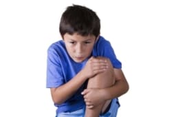 A young boy wearing a blue shirt holds leg in pain. Growing pains can make your child’s legs hurt and are common between the ages of 3 and 12. They are typically not serious.