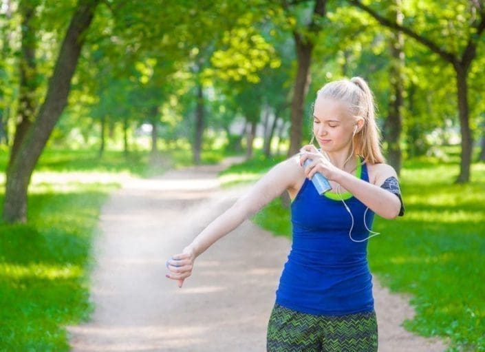 A young woman standing in a park while spraying insect repellents on skin before run.