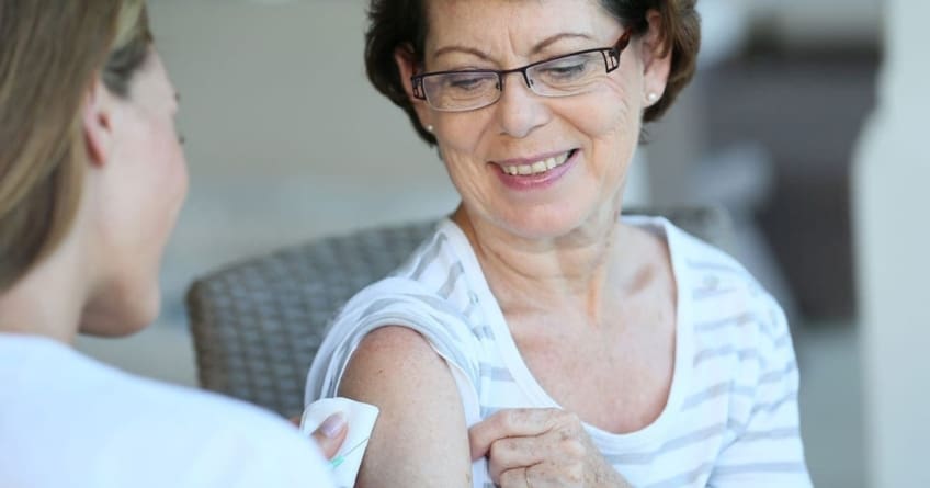 A medical professional prepares to give a vaccine to a an older woman patient.