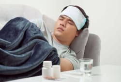 A sick man sleeps on the couch next to a table with medication and a glass of water. These days, when you’re feeling under the weather with a fever, body aches, and other symptoms, you may wonder whether you have season influenza (flu) or COVID-19. The two share many similarities, but there are a few differences.
