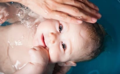 Baby boy being given a bath by his mother in a blue plastic bath bathtub.