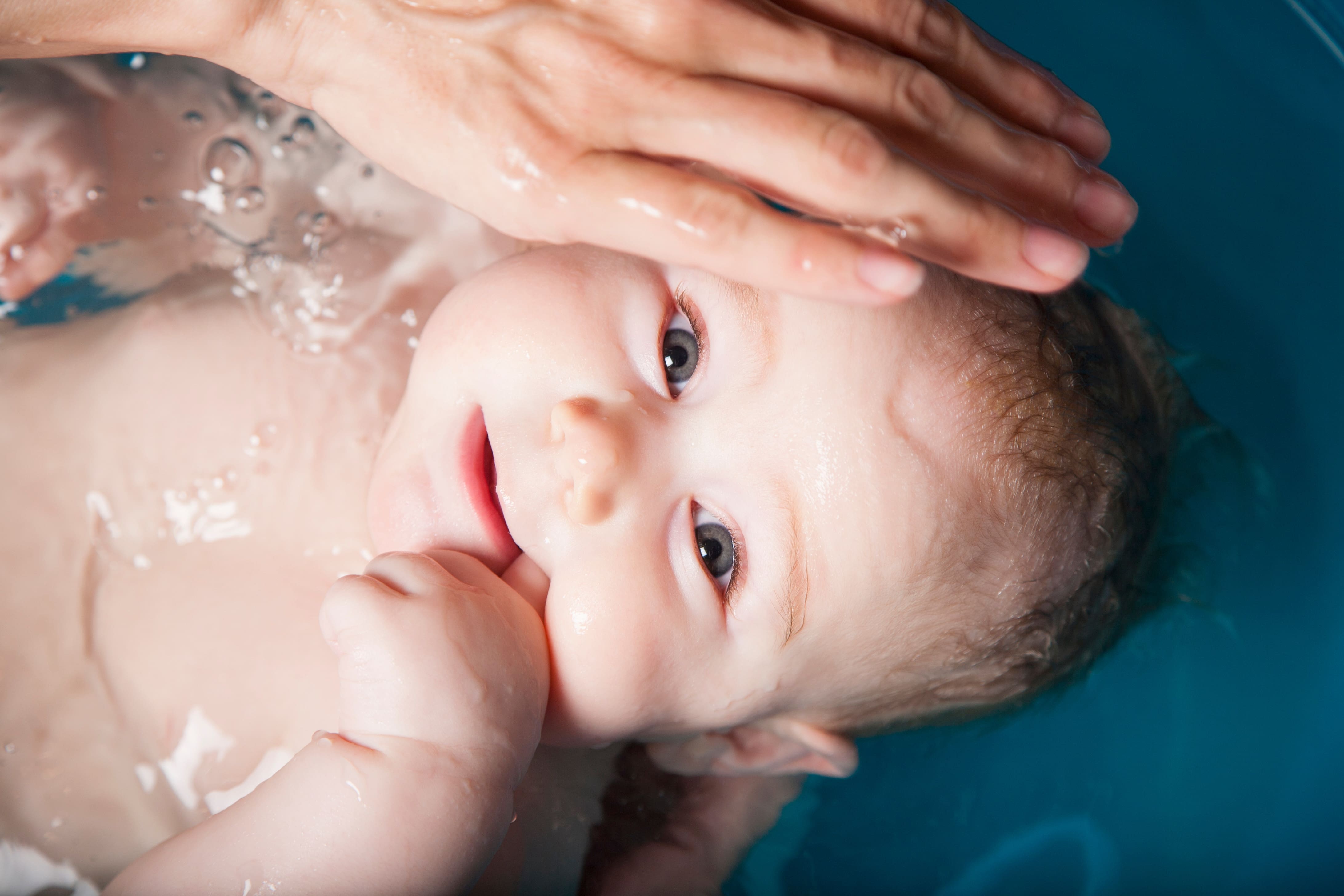 Baby boy being given a bath by his mother in a blue plastic bath bathtub.