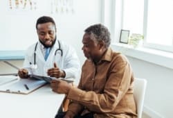 A doctor wearing a white coat sits with a patient in his office to go over the benefits of the RSV vaccine.