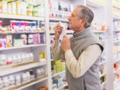 sick man holding tissue looks at OTC decongestants in a pharmacy
