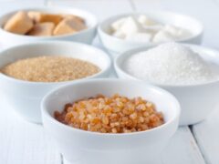 Five small white bowls, each filled with a different sugar substitute, sitting on a white table