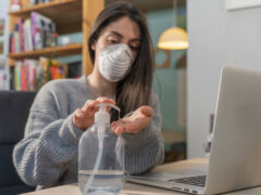 Coronavirus. Business woman working from home wearing protective mask. Business woman in quarantine for coronavirus wearing protective mask. Working from home. Cleaning her hands with sanitizer gel.