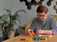 Activity can improve brain function. Elderly woman sitting at table and sorting jigsaw puzzle pieces, free space game