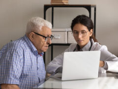 Close up female professional doctor consulting mature patient wearing glasses, using laptop, demonstrating medical checkup result, explaining prescription, treatment, healthcare service concept