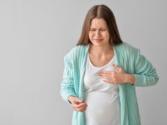 Ill pregnant young woman with pill on grey background
