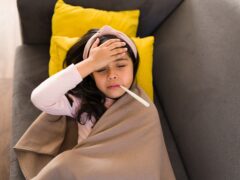 High angle of a latin girl with a thermometer on her mouth. Sick girl putting on hand on her forehead to check her temperature