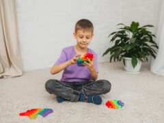 the boy sits on the floor and plays with a silicone toy, antistress. Pop is a sensory toy.