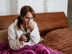 latin ill adult mature woman sneezing and using napkin for flu on bed at home in Mexico Latin America