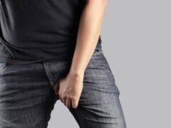 Asian man in reaction of scratching crotch on grey background, closeup. Annoying itch or Tinea Cruris. Human body problem or healthcare and medicine concept.