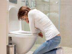 Woman, girl, experiencing sickness, vomiting, pregnancy, poisoning and morning discomfort, sitting over the toilet