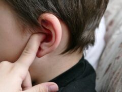 A child with an ear infection picks his ear with his finger, expressing that he is in pain.