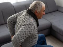 Elderly man near sofa with cactus at home. Hemorrhoids concept