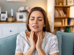 Close up of young woman rubbing her inflamed tonsils, tonsilitis problem, cropped. Woman with thyroid gland problem, touching her neck, girl has a sore throat