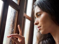 Thinking, lonely and woman in window by rain, winter weather and water with drops for gloomy atmosphere. Home, sad and female person with seasonal affective disorder, low energy and climate change