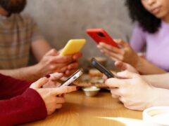 Close up of hands holding smartphones while sitting at table with food, highlighting phone addiction and lack of face to face communication during social gathering