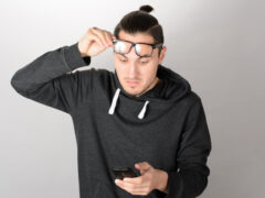Closeup portrait headshot middle aged man with glasses having trouble seeing cell phone screen because of vision problems. Bad text message. Negative human emotion facial expression feeling perception