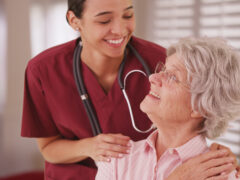 Hispanic female nurse looking and smiling with senior caucasian woman