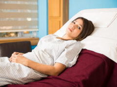 Pretty Hispanic woman looking concerned and sad while lying on a hospital bed