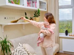 A woman dusts her shelf while carrying a baby