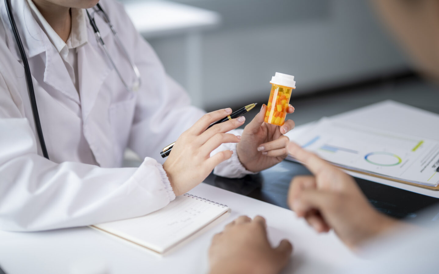 Doctor holding medicine bottle and pen, explaining prescription to patient
